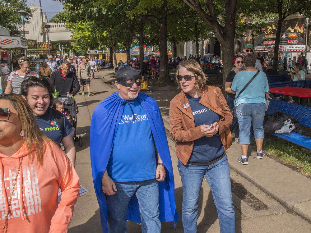 Minnesota's state demographer, Susan Brower (center), walks with Dean Goldberg, donning a blue cape and black mask as 