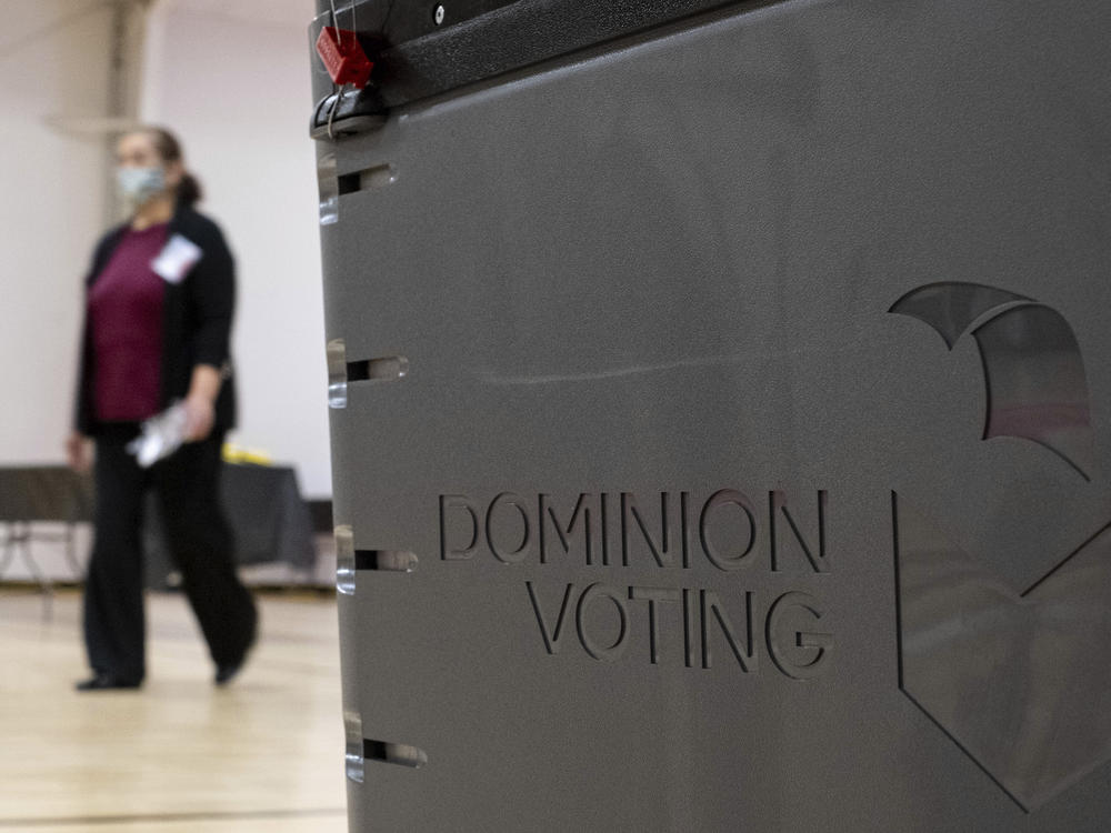 A worker passes a Dominion Voting Systems ballot scanner during Georgia's runoff Senate elections in January in Gwinnett County outside Atlanta. Former President Donald Trump and his allies spread falsehoods about the company's role in the 2020 election, leading to a slew of defamation lawsuits.