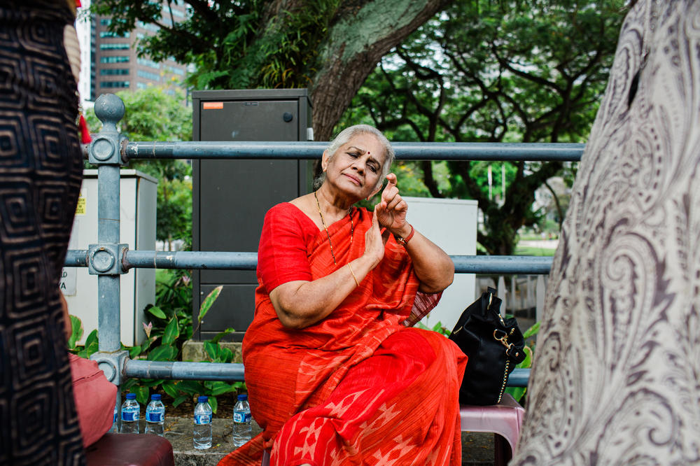 Indian dance pioneer Santha Bhaskar demonstrates a scene depicting the beauty of nature, petting a bird, for her daughter and granddaughters. She shows them the dance gestures and expressions as she prepares to perform for a government event.