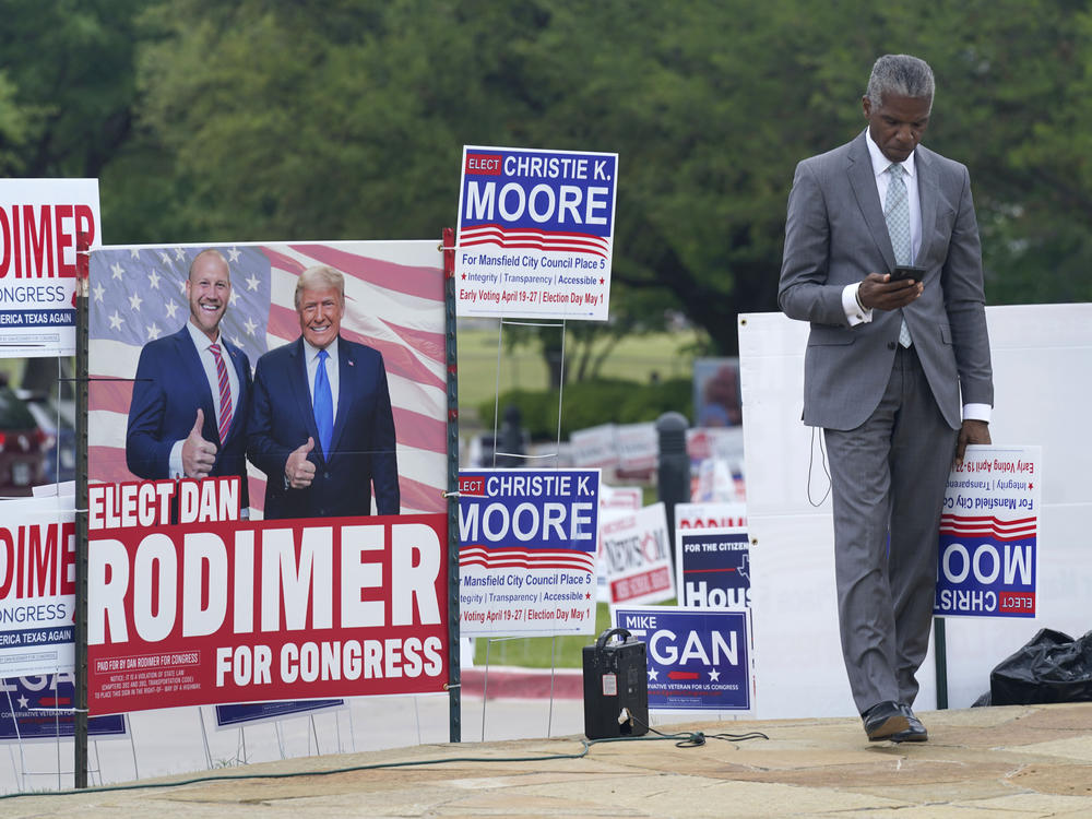 Volunteer Al Green looks at his phone as he takes a break from holding a sign supporting his candidate in a local election outside an early voting location Tuesday, April 27, 2021, in Mansfield, Texas.