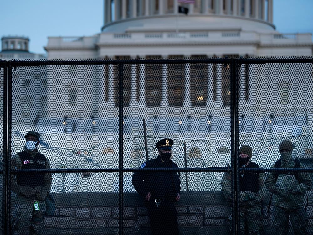A Capitol Police officer stands with members of the National Guard behind a fence surrounding the Capitol on Jan. 7, a day after the insurrection.
