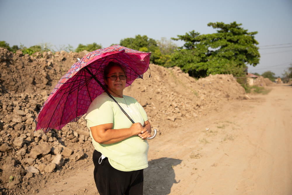 Maria Jimenez stands in front of one of the many piles of dried mud that bulldozers have moved to restore access to her neighborhood in La Lima, five months after the hurricanes.