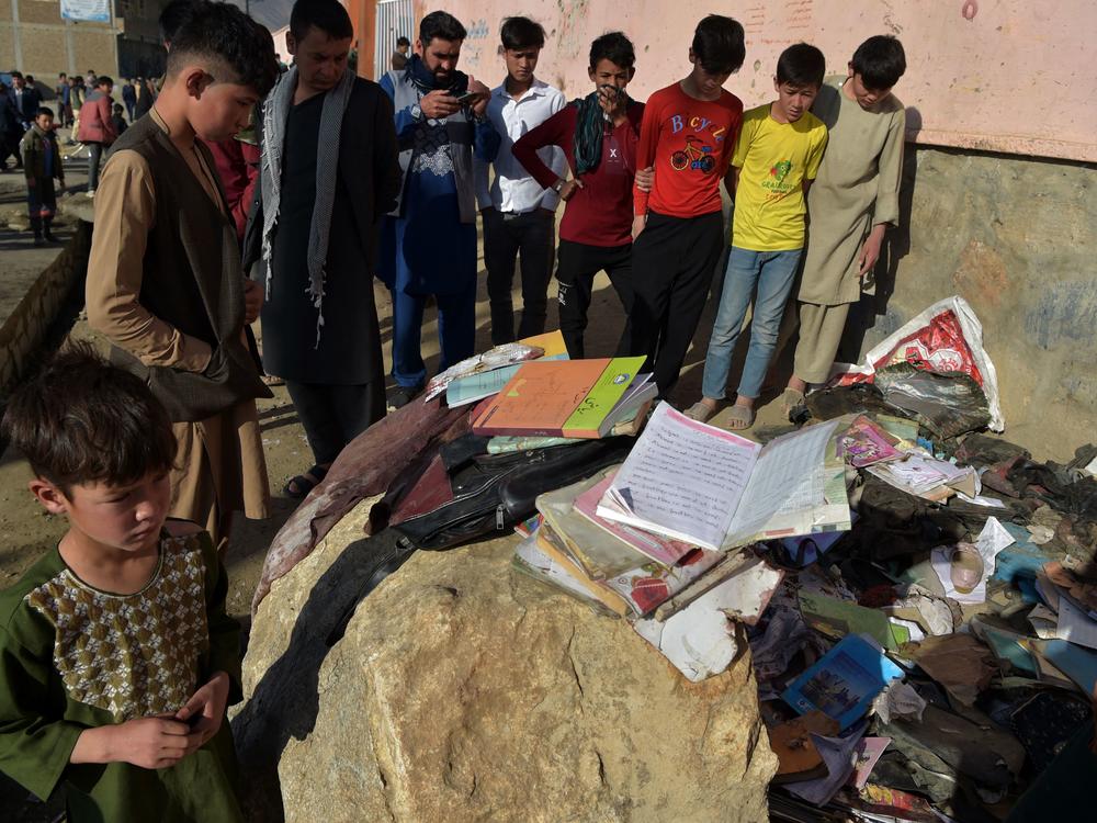Onlookers stand next to the backpacks and books of victims of the bombing Saturday in Kabul. Most of the victims were teenage schoolgirls.