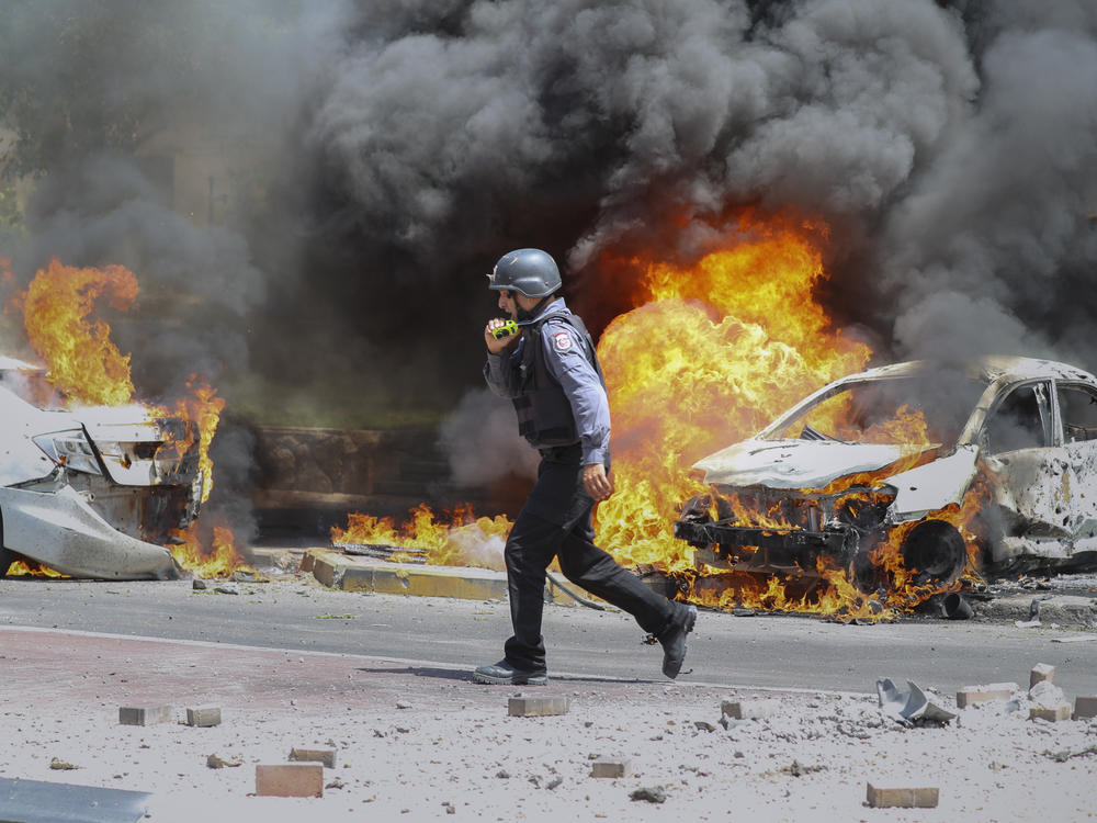 An Israeli firefighter walks next to cars hit by a rocket fired from Gaza on Tuesday in the southern Israeli city of Ashkelon.