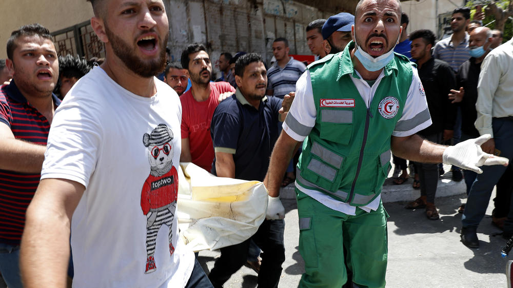 Medics and youths chant slogans while carrying the covered body of a man who Palestinian officials say was killed in Israeli airstrikes on his apartment building Tuesday in Gaza City.