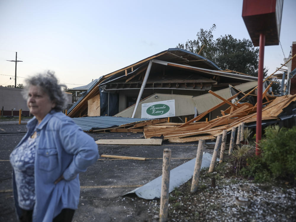 A woman stands in front of a destroyed restaurant after Hurricane Zeta on Oct. 29, 2020, in Chalmette, La. In a postseason analysis, NOAA upgraded Zeta's windspeeds, saying it was a 