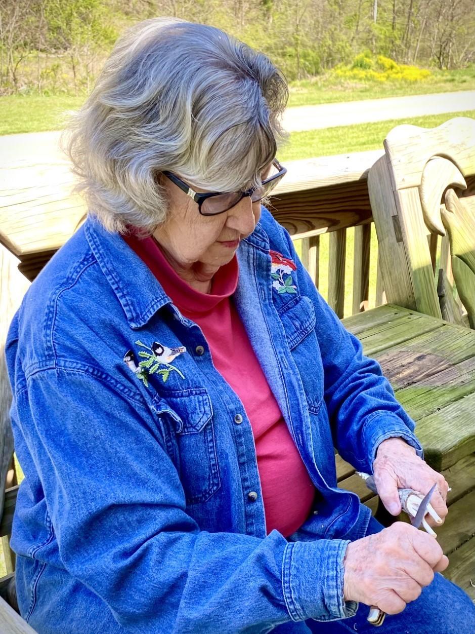 Minnie Adkins sits on her porch in rural eastern Kentucky, using her pocket knife to whittle a rooster from a piece of Maplewood.