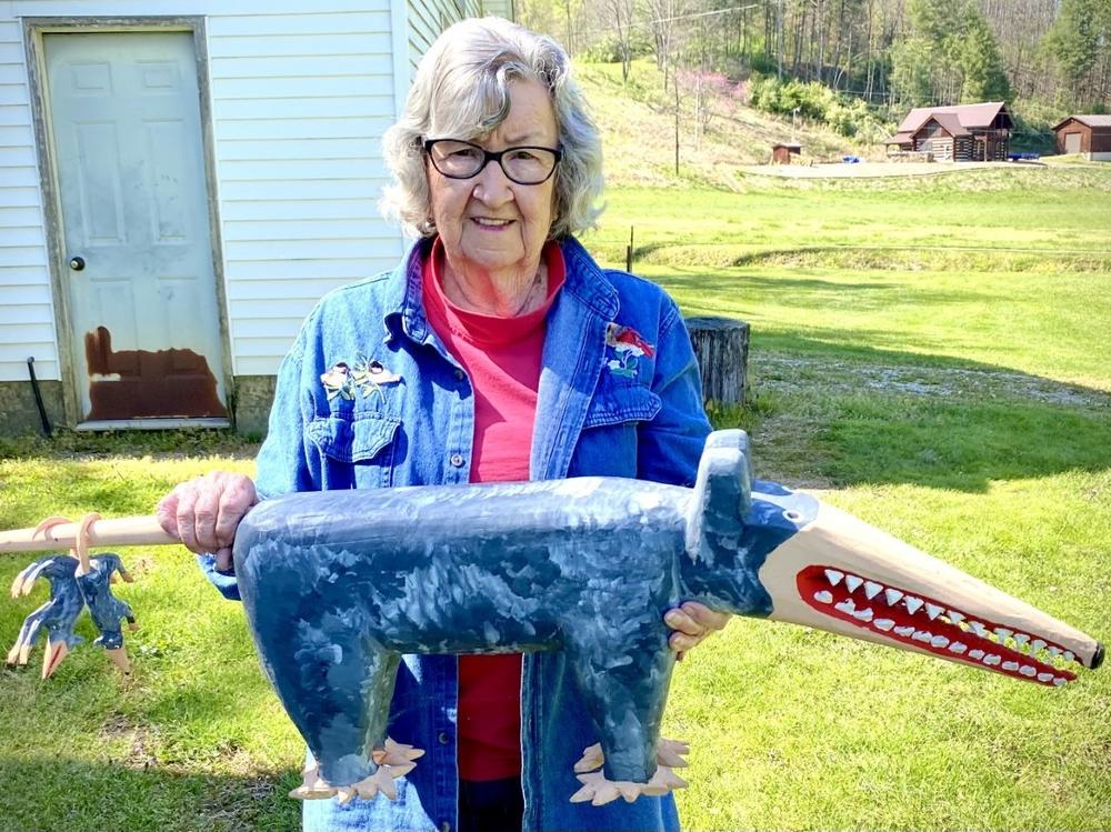 Minnie Adkins stands in her yard in Elliott County, Ky., holding her carving of a possum with baby possums dangling on its tail.