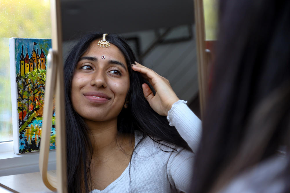 Kriti Sarav gazes in the mirror after applying a bindi on her forehead and a maang tikka along the parting of her hair.