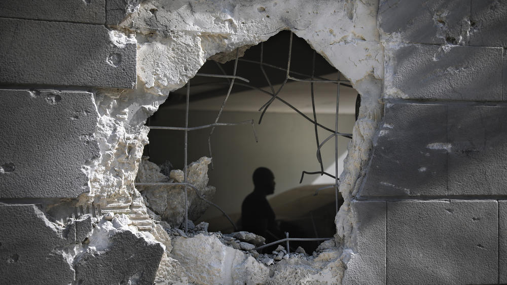A man is seen through a hole in the wall of a residential building after a rocket fired from the Gaza Strip struck Friday in Ashkelon, Israel.