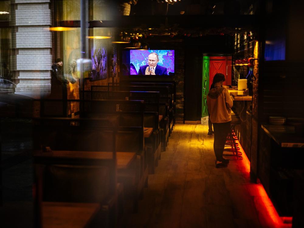 Through a restaurant window, a TV screen shows Russian President Vladimir Putin addressing his annual news conference, in Moscow on Dec. 17, 2020.