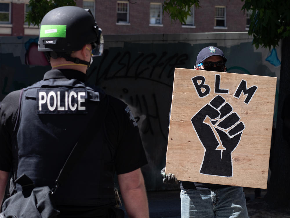 A police officer stands in front of a Black Lives Matter sign during a protest in front of Seattle City Hall on August 9, 2020.