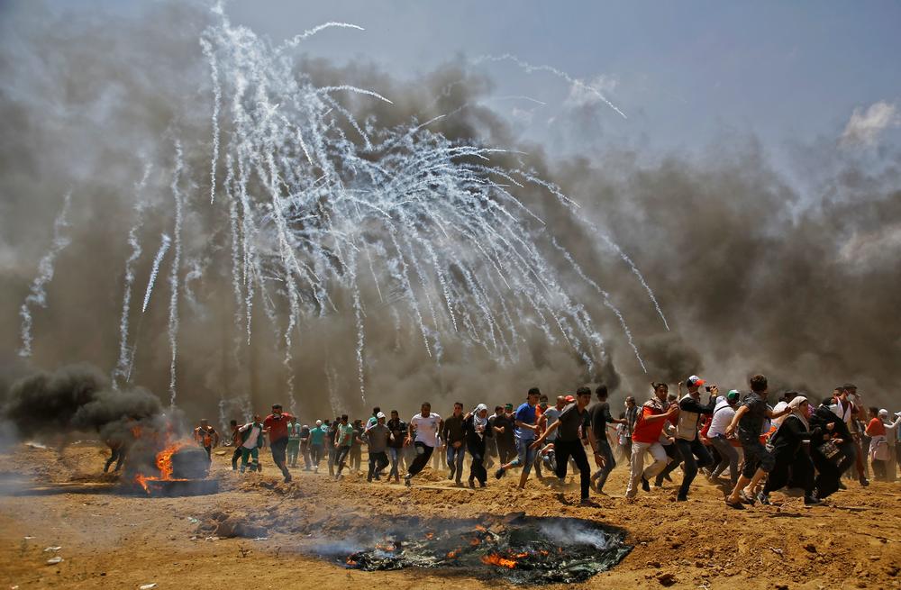 Palestinians run for cover from tear gas launched by Israeli security forces near the border between Israel and the Gaza Strip, east of Jabalia, on May 14, 2018, as Palestinians protest over the inauguration of the U.S. Embassy following its controversial move to Jerusalem.