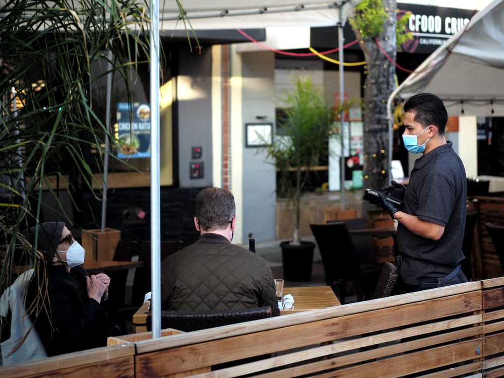 A staff member wearing a mask serves customers at a restaurant in San Mateo, Calif., on May 17.