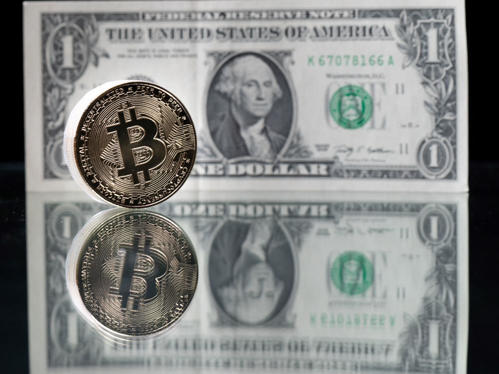 A physical imitation of the Bitcoin cryptocurrency is pictured with a $1 bank note. Cryptocurrencies are plunging over a range of factors, including the spillover impact from falling stock markets and fears about increased regulations.