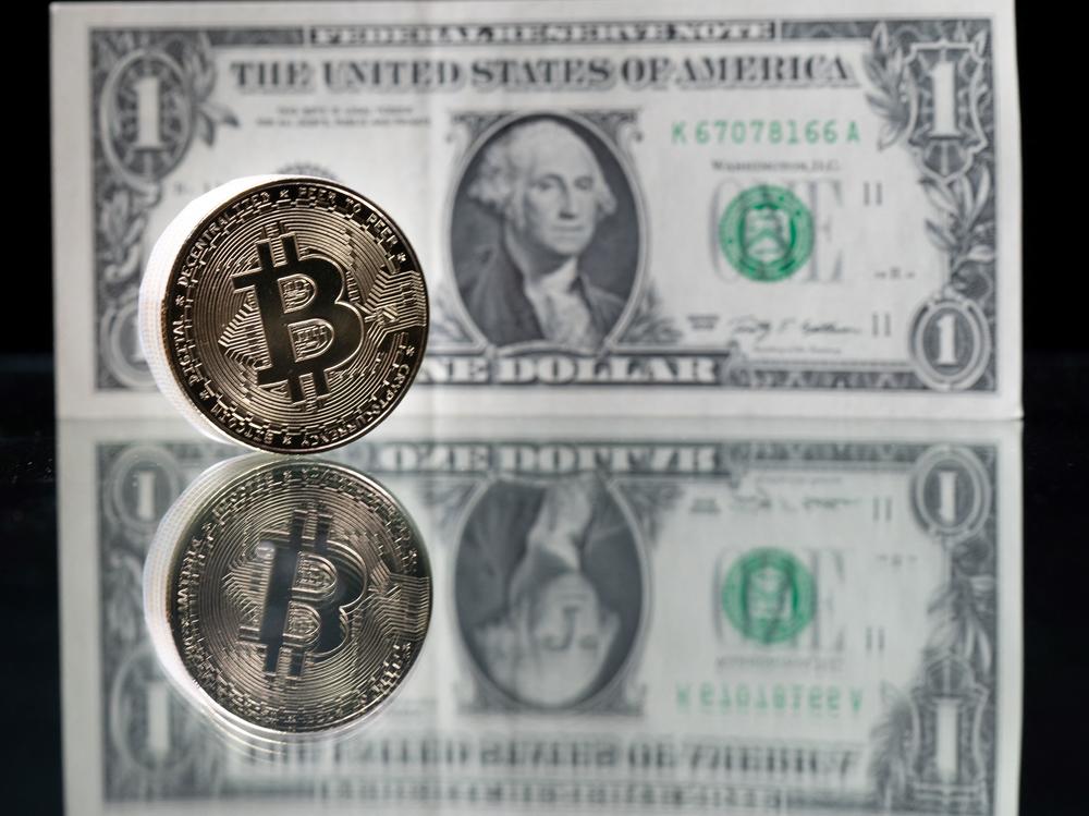 A physical imitation of the Bitcoin cryptocurrency is pictured with a $1 bank note. Cryptocurrencies are plunging over a range of factors, including the spillover impact from falling stock markets and fears about increased regulations.