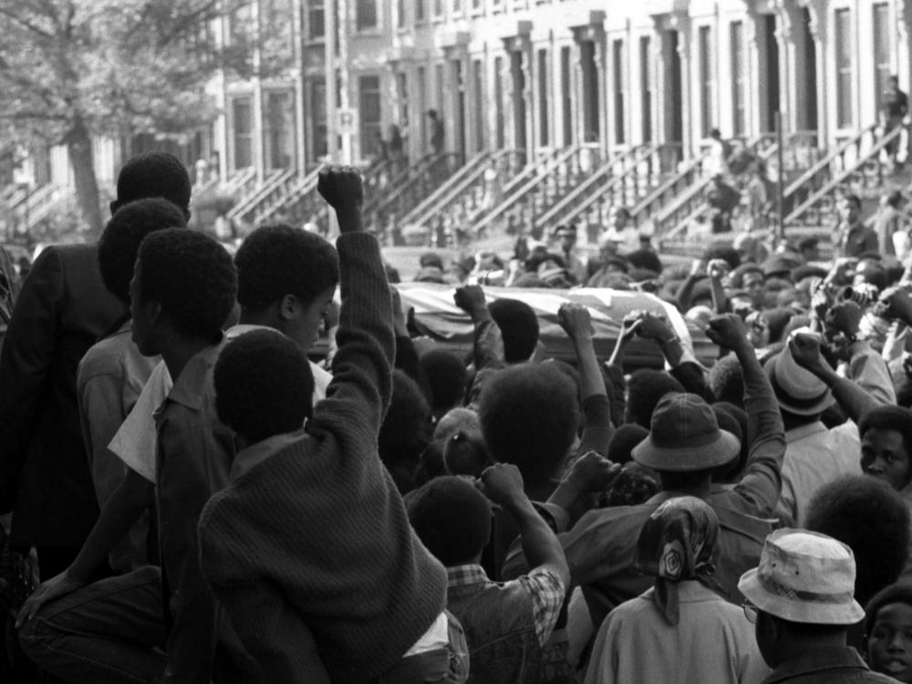 On a Brooklyn street in September 1971, a sea of fists greets the caskets of several of the incarcerated men killed in the violent clash at Attica Correctional Facility that month.