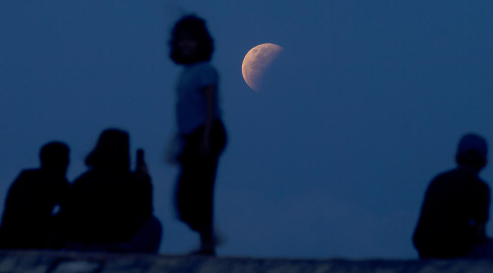 Residents watch the lunar eclipse Wednesday at Sanur beach in Indonesia's Bali. The reddish-orange color of the supermoon is the result of all the sunrises and sunsets in Earth's atmosphere projected onto the surface of the eclipsed moon.