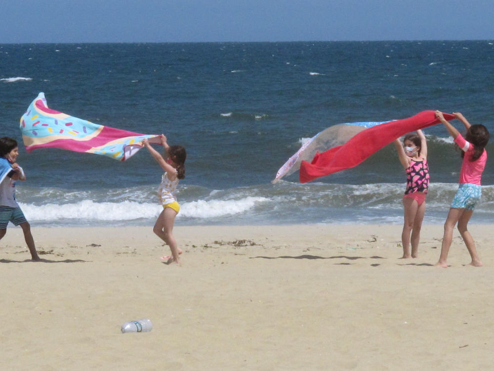 Children play with beach towels on a windy day in Belmar, N.J., on Tuesday. Millions are expected to hit the road or board a plane to celebrate Memorial Day weekend as more people get vaccinated and COVID-19 restrictions are scaled back.