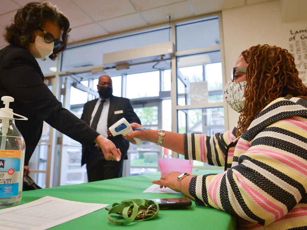 Yvette Richards, director of community connection at St. James United Methodist Church in Kansas City, Mo., checks temperatures before Sunday morning services. The church is hosting vaccination clinics and holding socially distanced services after shutting down for much of the pandemic.