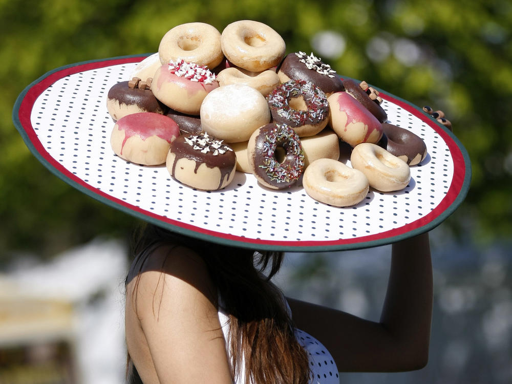 A woman, likely a doughnut/donut-lover, wears a hat resplendent in deep-fried goodies.