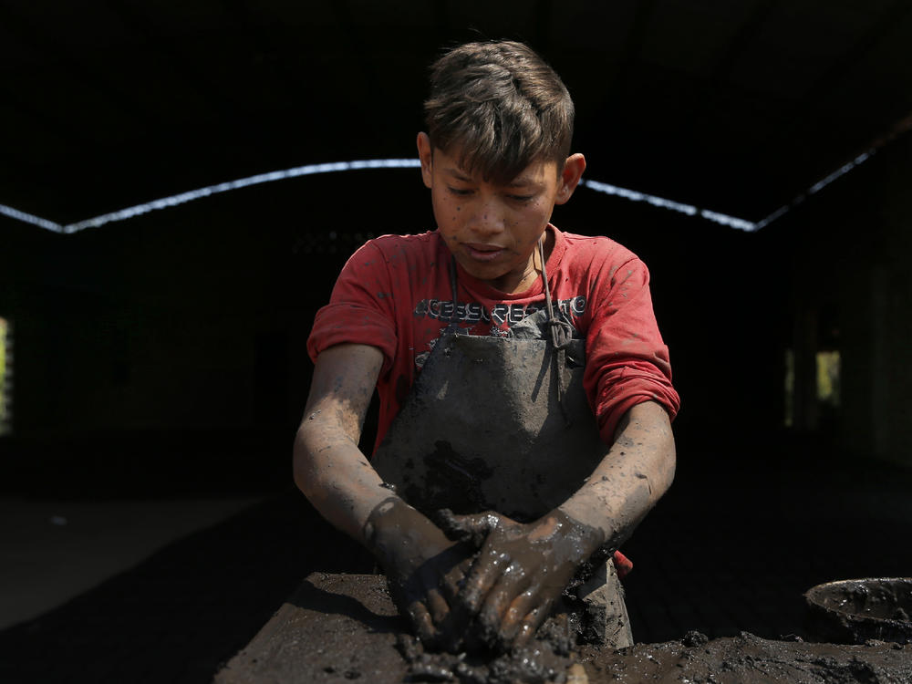 Cesar, 13, places clay in a mold to make bricks at a factory in Tobati, Paraguay.