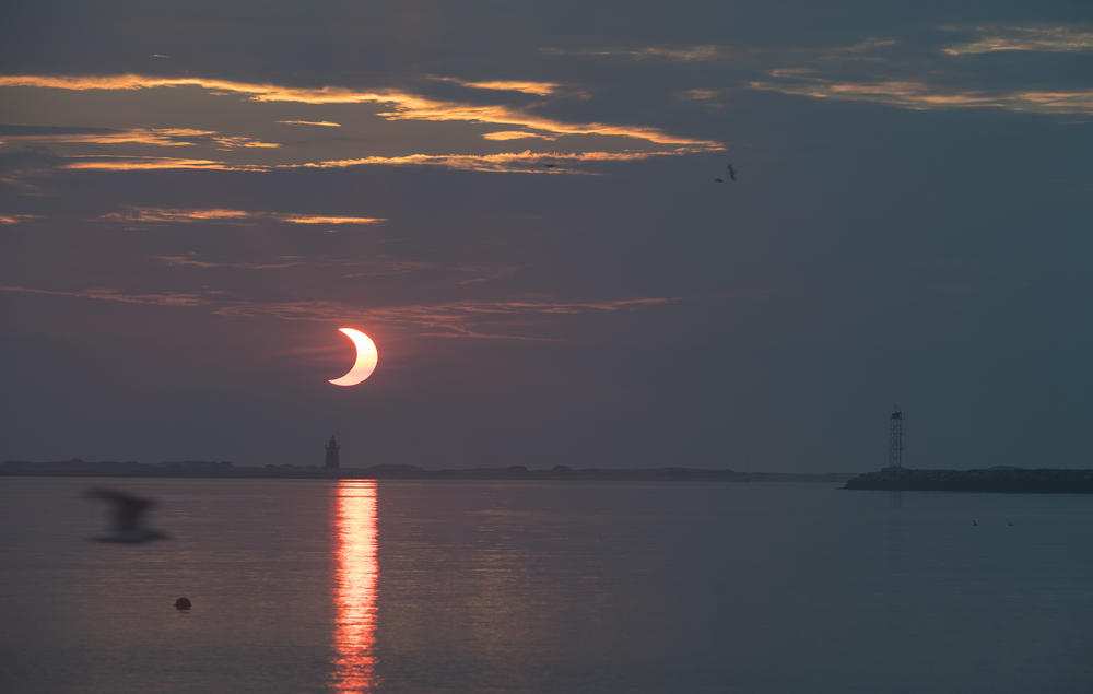 In this image provided by NASA, a partial solar eclipse is seen as the sun rises behind the Delaware Breakwater Lighthouse in Lewes, Del.