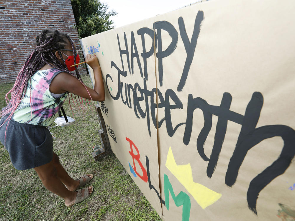 A girl paints on a poster celebrating Juneteenth in downtown Jackson, Miss., on June 19, 2020. Congress has voted to make the day a federal holiday.