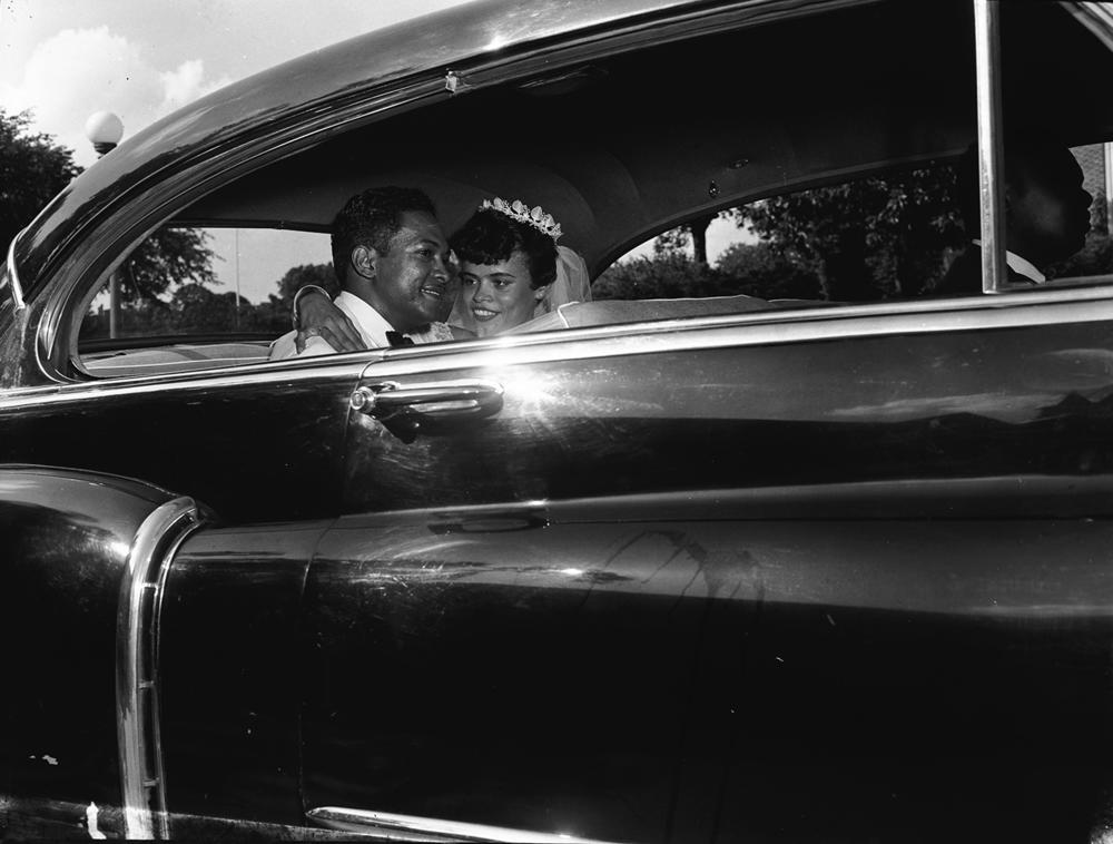 A bride and groom sit in a car.