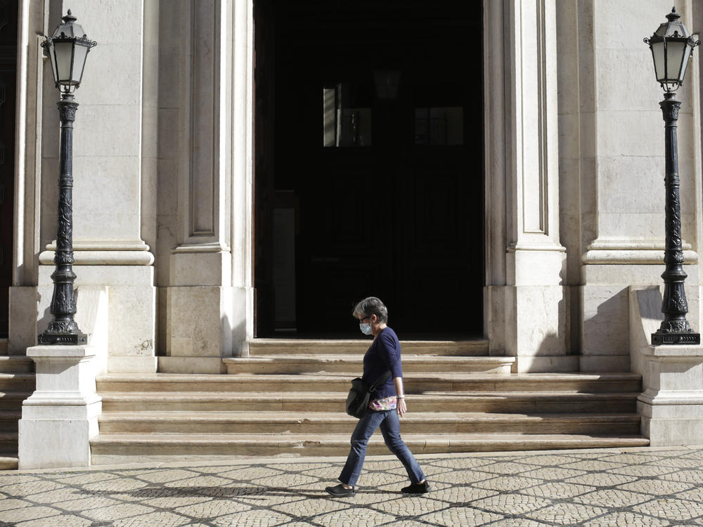 A woman wearing a face mask walks past a church in Lisbon's Chiado neighborhood on Thursday. The Portuguese government is returning to some lockdown measures due to a surge in cases linked to the COVID-19 delta variant.