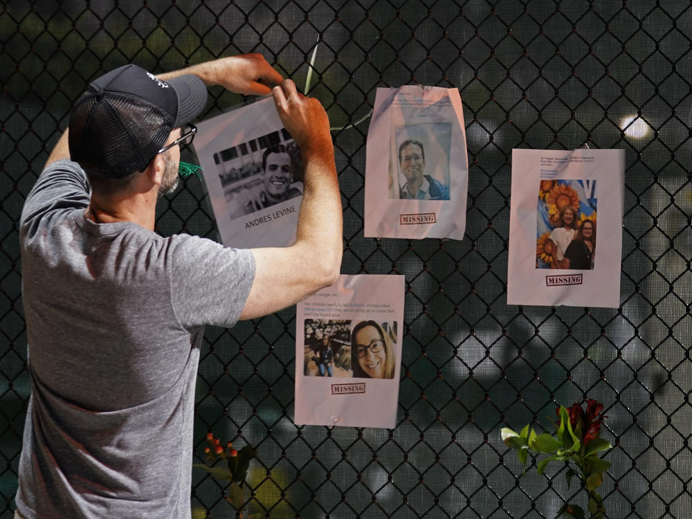 A man hangs a photo of a missing person on a fence near the site of the oceanfront condo building that partially collapsed in Surfside, Fla.