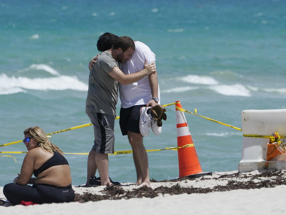 Two men console each other on the beach Sunday near the site of the Champlain Towers South condo building in Surfside, Fla. Rescuers kept digging through the mound of rubble over the weekend, clinging to hope that someone could be found alive.