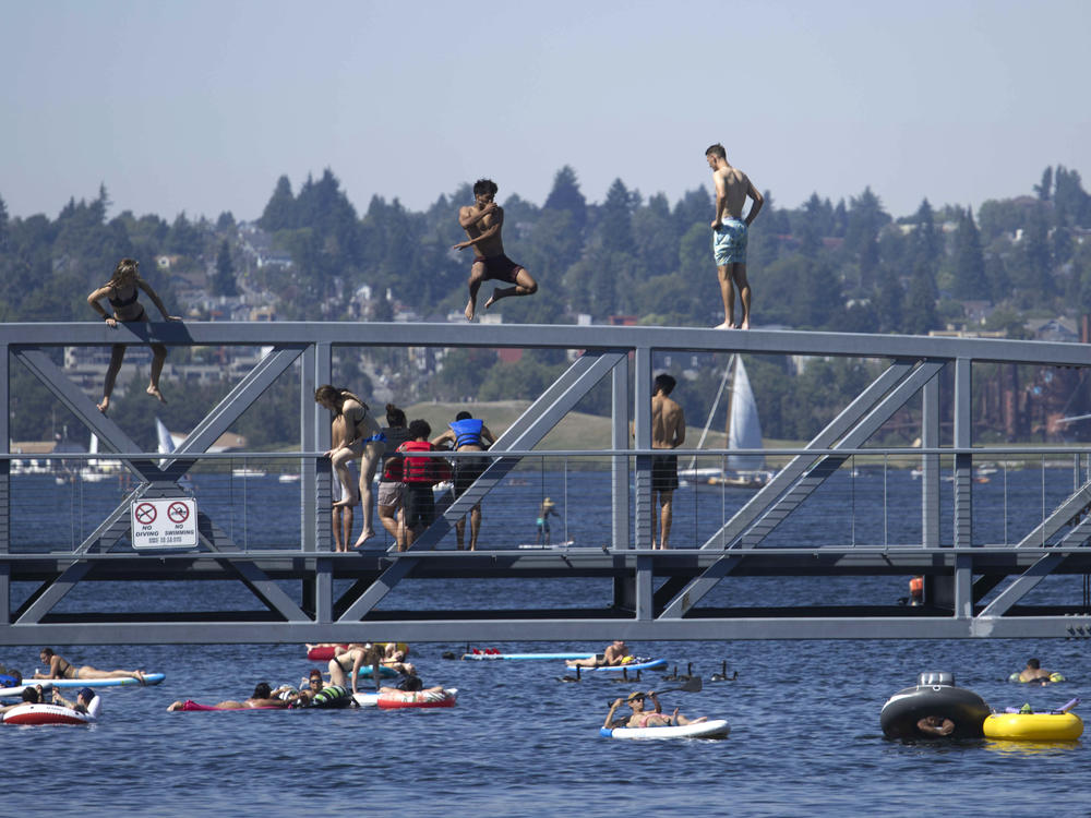 People jump from a pedestrian bridge at Lake Union Park in Seattle on Sunday as a record-setting heat wave blasts the Pacific Northwest.