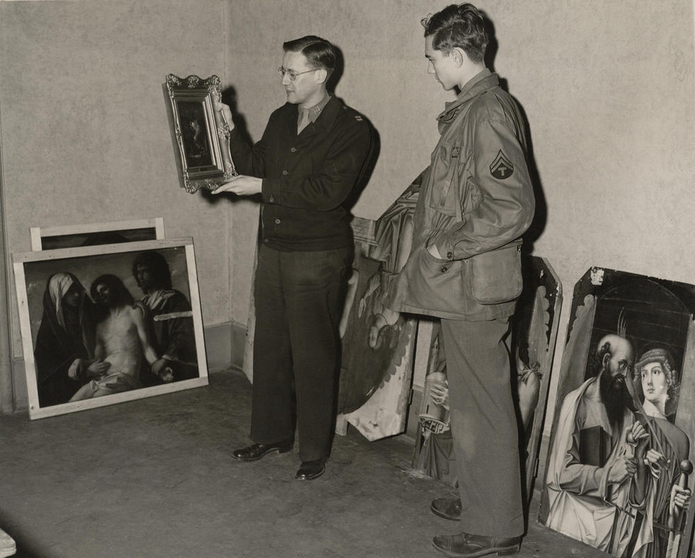 Walter Farmer holding a painting at Wiesbaden Central Collecting Point, Lindsay C. Kenneth Papers, Special Collections, Binghamton University Libraries