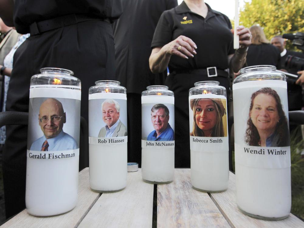 In this June 29, 2018, file photo, pictures of five employees of the <em>Capital Gazette</em> newspaper adorn candles during a vigil across the street from where they were slain in the newsroom in Annapolis, Md.