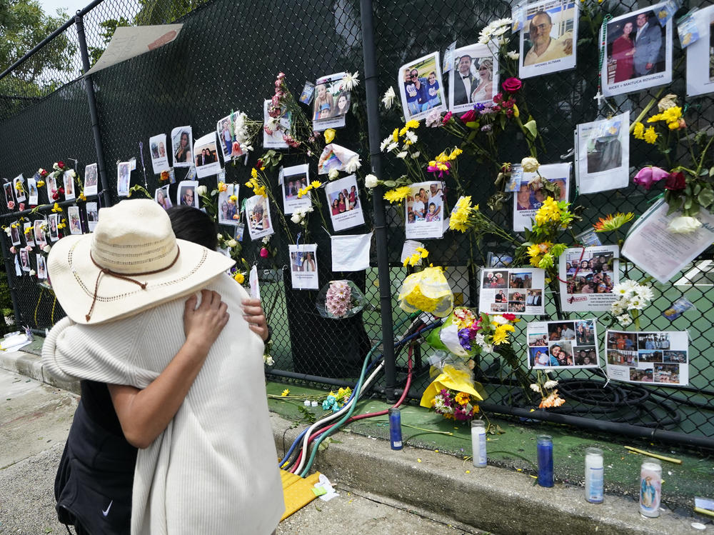 People embrace Monday at a makeshift memorial outside St. Joseph's Catholic Church in Surfside, Fla., near the site of the Champlain Towers South condo that partially collapsed last week.