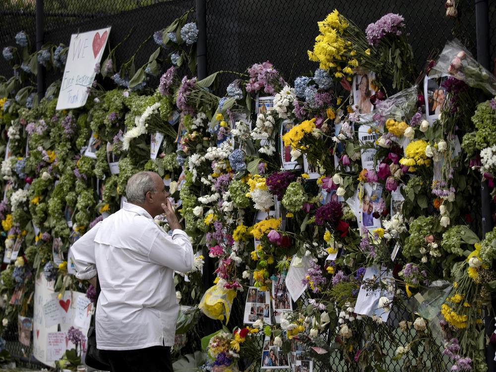 A man looks at a memorial Tuesday with pictures of some of the missing from the partially collapsed 12-story Champlain Towers South condo building in Surfside, Fla.