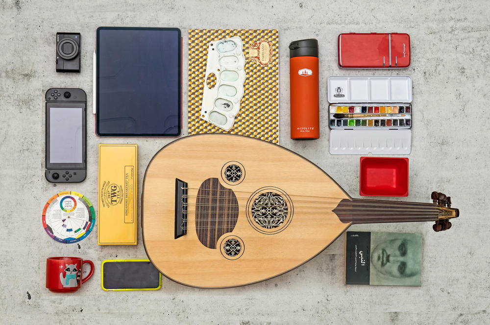 Items left to right, top to bottom: Camera, Nintendo Switch, color wheel, mug, tablet, tea, phone, supplies for watercolor paintings, Turkish oud, water bottle, pencil case, watercolor paints, book.