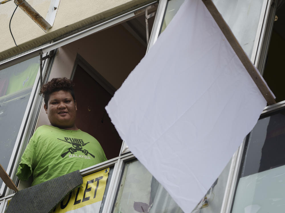Mohamad Nor Abdullah, born without arms, looks out from a window near a white flag outside the window of his rented room in Kuala Lumpur, Malaysia on July 3. When Mohamad Nor put a white flag outside his window late at night, he didn't expect the swift outpouring of support. By morning, dozens of strangers knocked on his door, offering food, cash and encouragement.