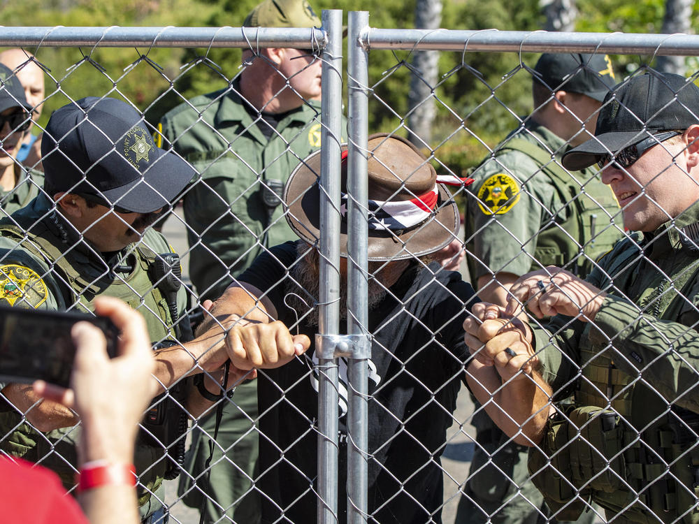 Sheriff's deputies eventually had to cut hand-shaped holes in the fence to handcuff and arrest Alan Hostetter.