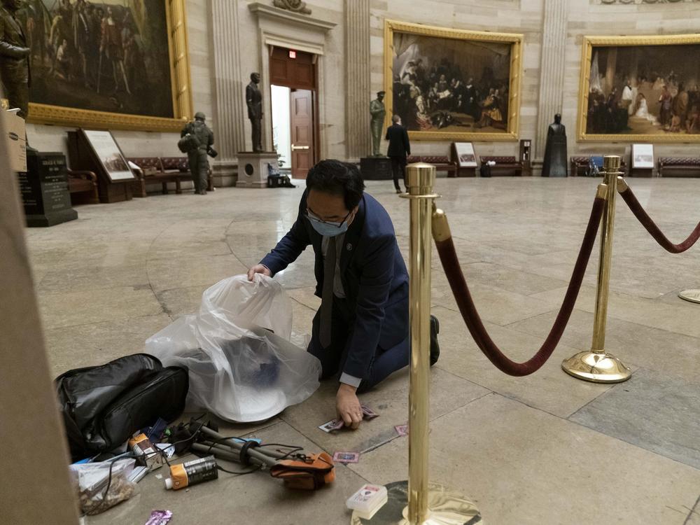 Rep. Andy Kim, D-N.J., cleans up debris and personal belongings strewn across the floor of the Rotunda in the early morning hours of Thursday, Jan. 7, 2021, after protesters stormed the Capitol in Washington, on Wednesday. (AP Photo/Andrew Harnik)