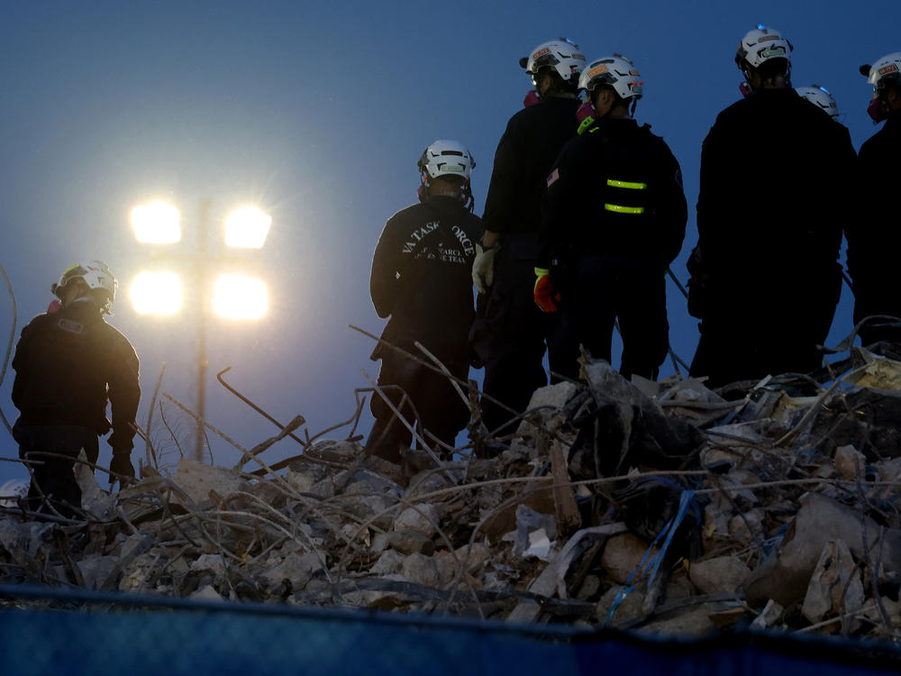 Workers oversee an excavator dig through the rubble of the collapsed 12-story Champlain Towers South condo building on Friday.