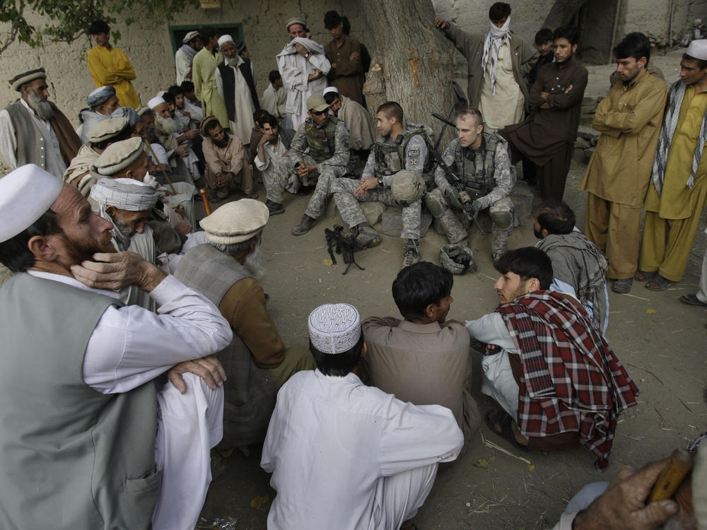 An American lieutenant, center, meets with villagers in Afghanistan's Kunar province in 2009, assisted by an interpreter, sitting to his right wearing a baseball cap. The U.S. will begin the evacuation of some 18,000 Afghan nationals who aided military operations, along with their families, in late July.