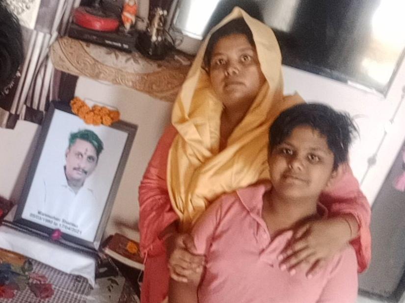 Pooja Sharma (center) and her two daughters, Lata, 14, and Yukti, 12, sit in front of a portrait of Sharma's late husband and the girls' father, Manmohan. He died from COVID-19 in April, leaving Sharma to fend for her family by herself.