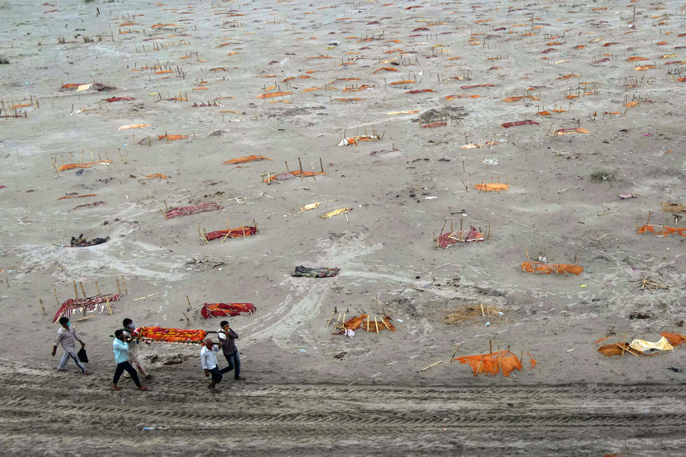 Relatives carry a body for cremation past corpses partially exposed in shallow sand graves. In May, rains washed away the top layer of sand at a cremation ground on the banks of the Ganges River in Shringverpur, India.