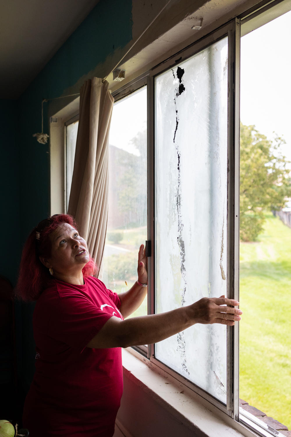 María Lara shows a loose and broken window in her home. She says she is afraid it will fall and hurt her daughter.