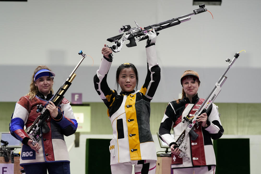 Qian Yang holds her rifle aloft after winning a gold medal. Anastasiia Galashina (left) of the Russian Olympic Committee took the silver medal and Nina Christen of Switzerland took the bronze medal.