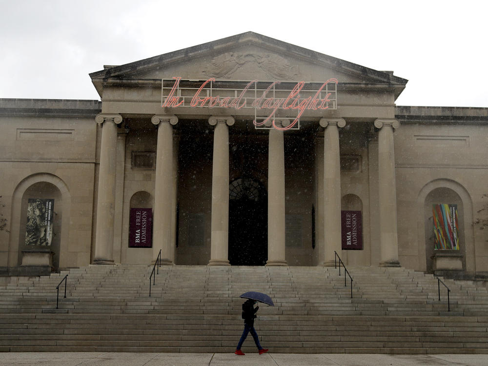 A man covers himself from rain with an umbrella as he walks by the Baltimore Museum of Art on April 21, 2020. An upcoming exhibit at the museum will be curated by security guards.