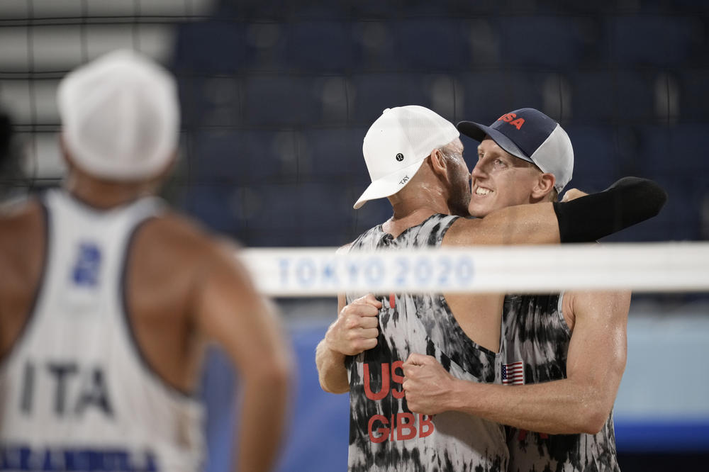 Jake Gibb (center) hugs new teammate Tri Bourne after winning a men's beach volleyball match against Italy on Sunday in Tokyo.