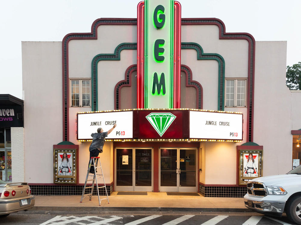 Kenny Nations, manager of the movie theater, changes the sign on the marquee; he is fully vaccinated and has tried to encourage co-workers to follow suit.